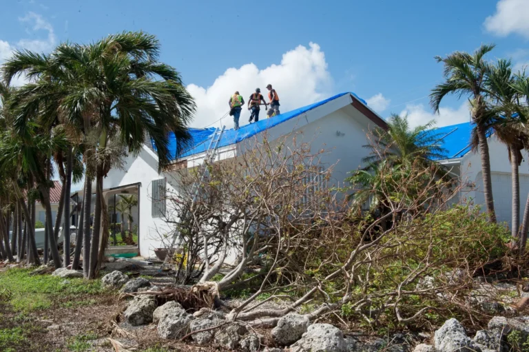 Storm damage insurance claim: workers install a blue tarp on a hurricane-damaged roof in Florida